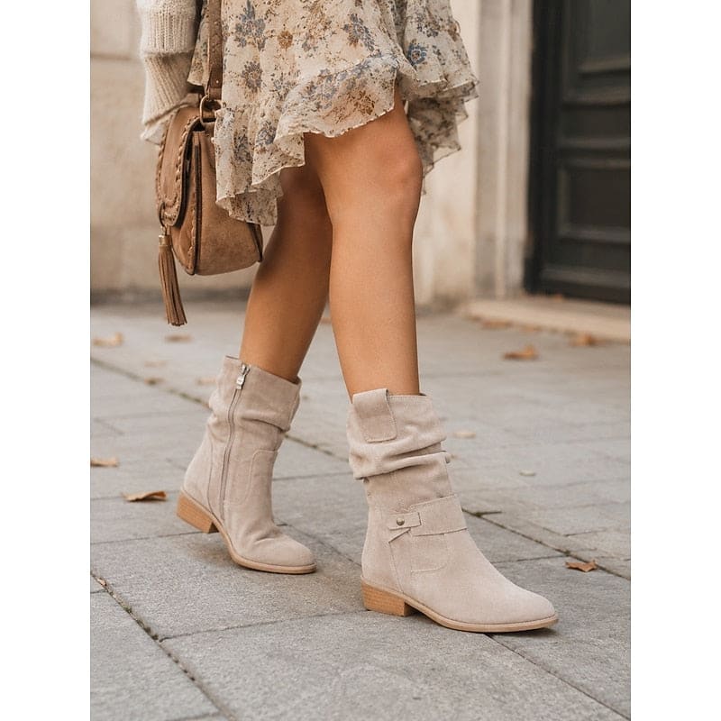 Kvinde bærer beige ankelstøvler med slouchy skaft, blokhæl og spændedetalje på flisegulv._1