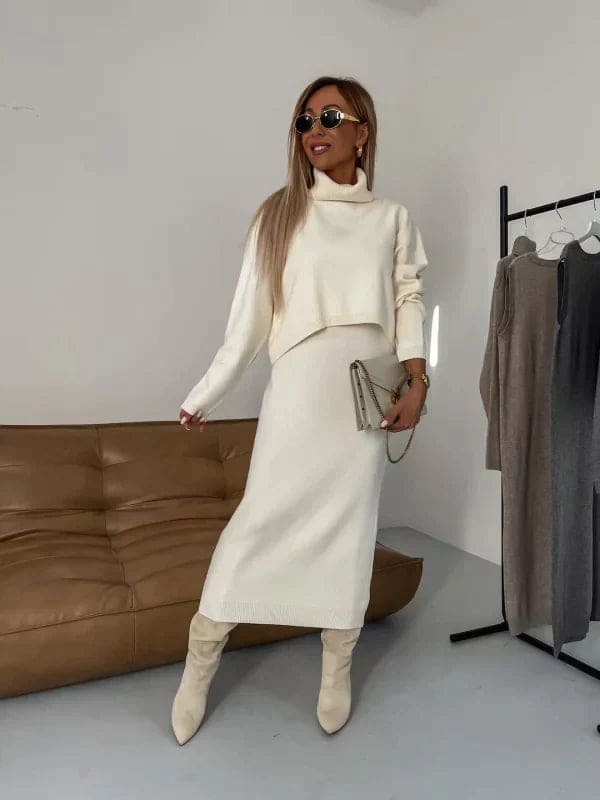 Model iført et hvidt strikket co-ord sæt bestående af en cropped jumper med høj hals og en lang nederdel, stylet med beige støvler og solbriller_0