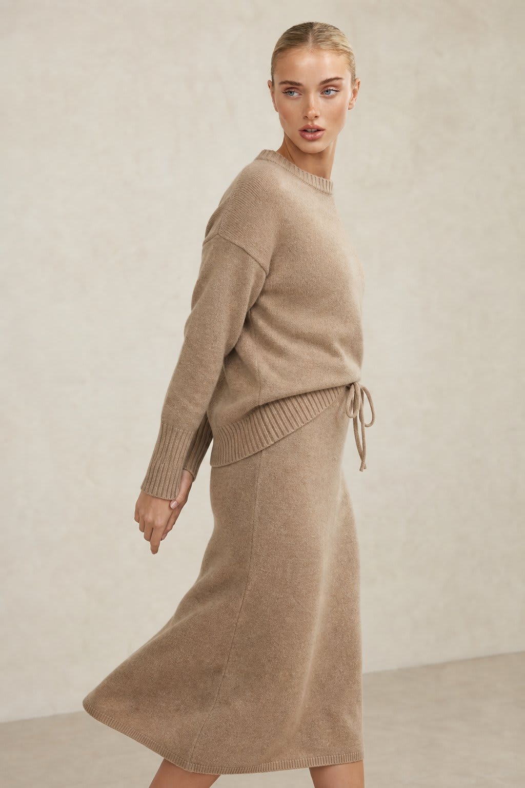 Model iført beige strikket sæt bestående af løstsiddende sweater og matchende nederdel med sliddetalje_0