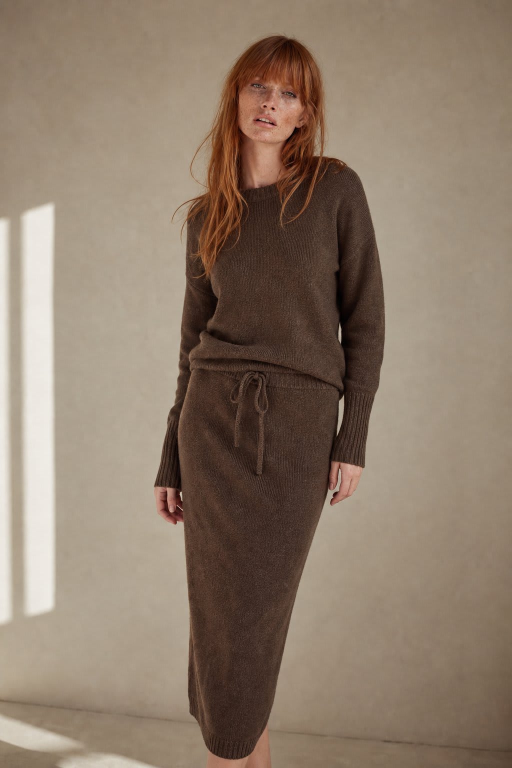 Model iført beige strikket sæt bestående af løstsiddende sweater og matchende nederdel med sliddetalje_2
