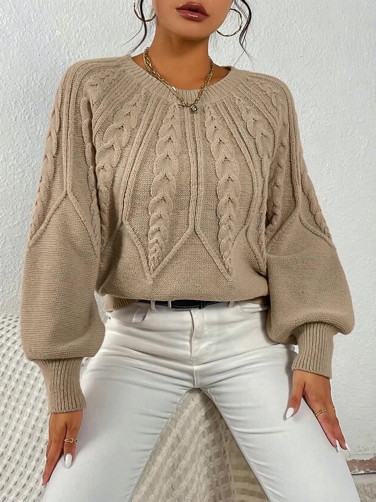 Kvinde iført sort strikket sweater med kabelstrik og ballonærmer, stylet med hvide bukser og halskæde, fotograferet forfra_10