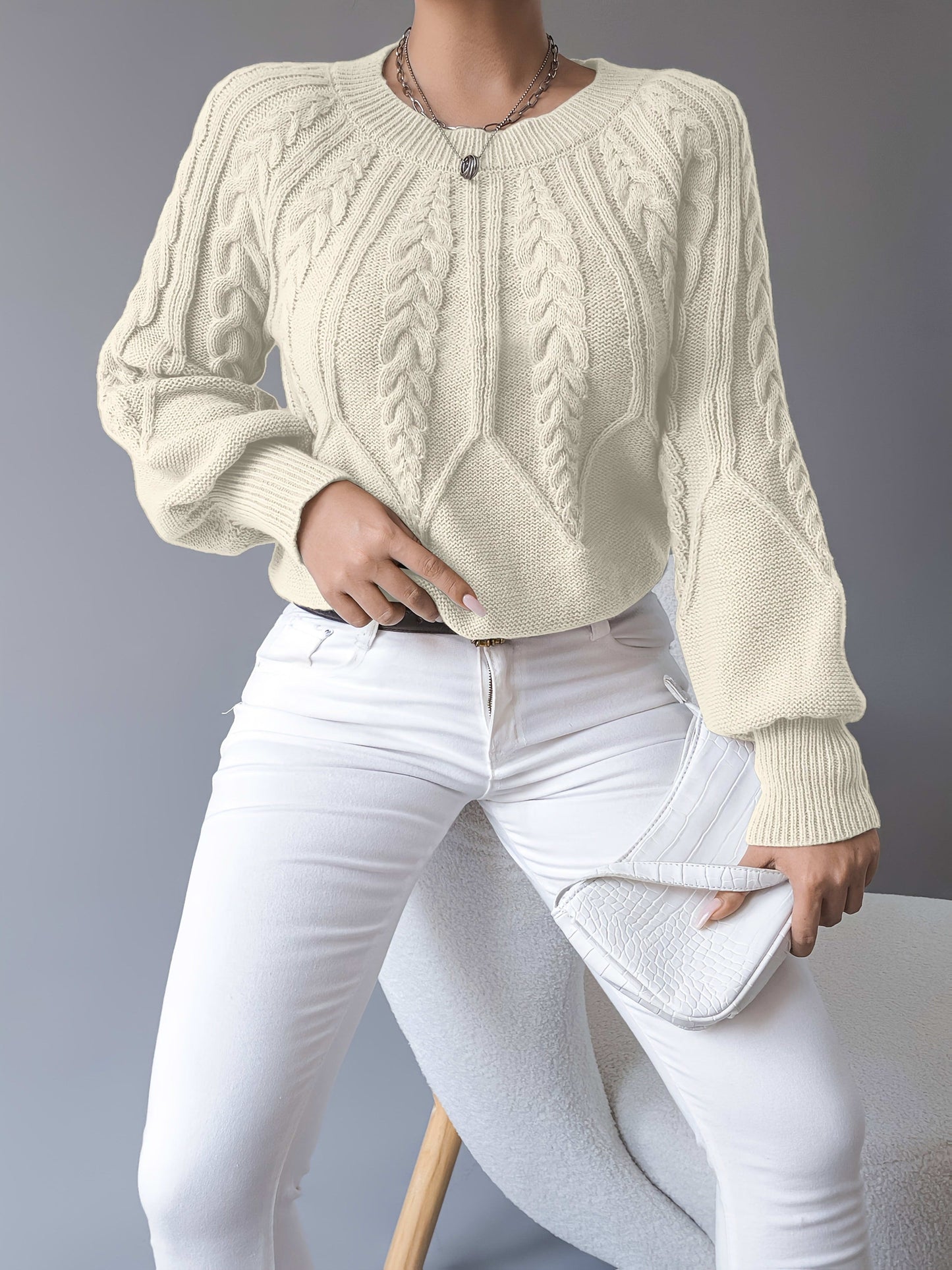 Kvinde iført en beige strikket sweater med kabelmonster og ballonærmer kombineret med hvide bukser_10