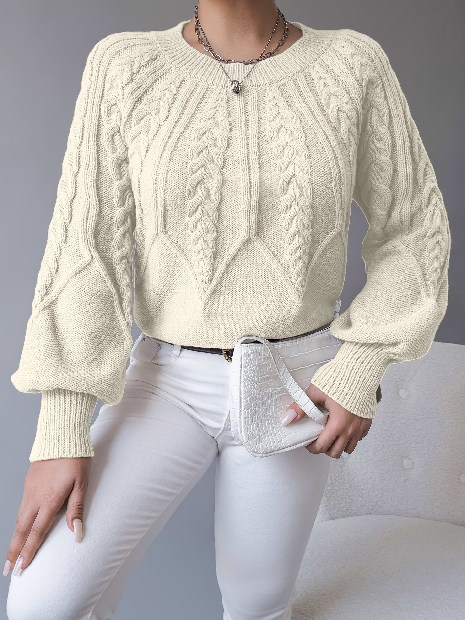 Kvinde iført en beige strikket sweater med kabelmonster og ballonærmer kombineret med hvide bukser_11