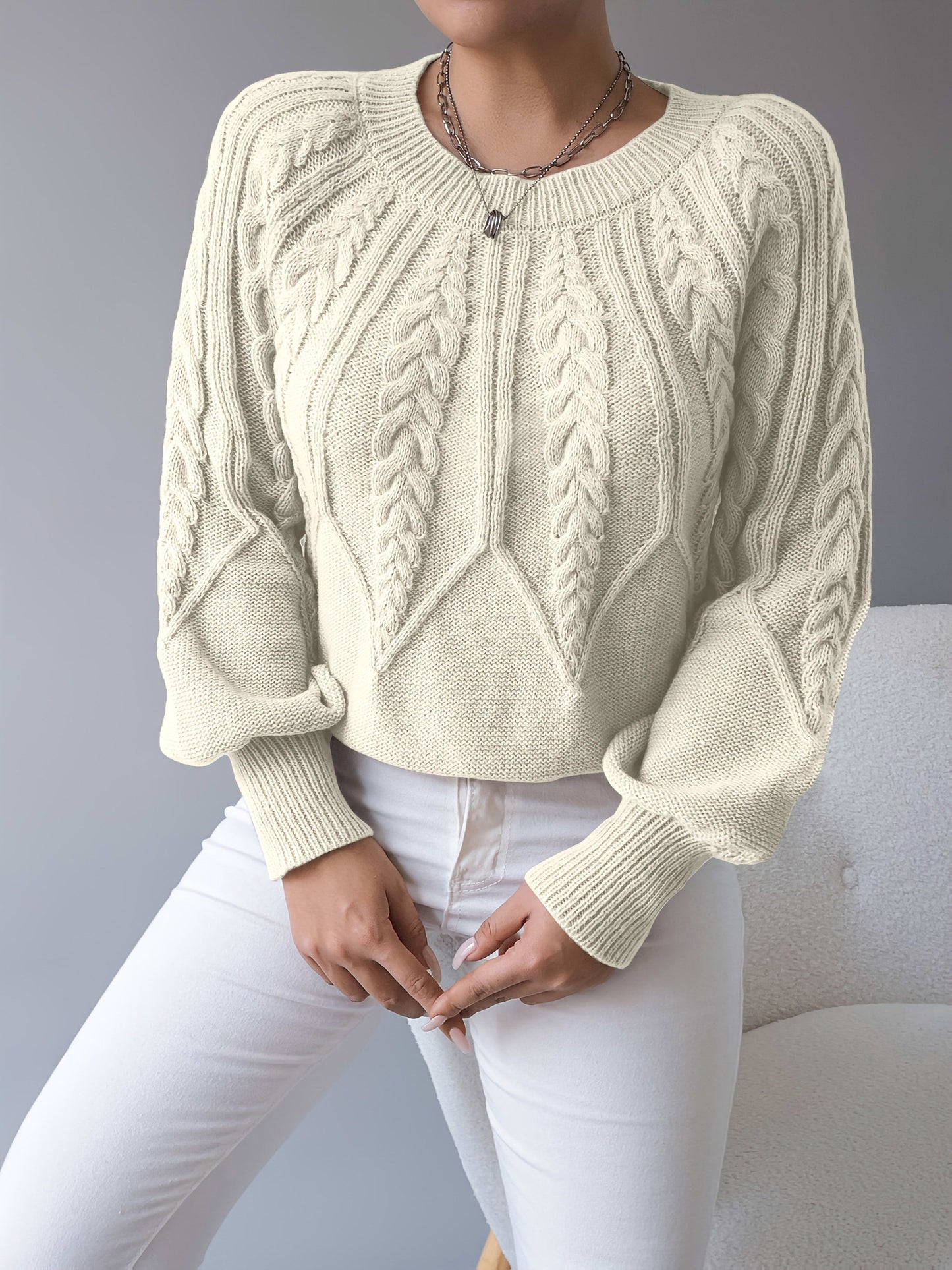 Kvinde iført en beige strikket sweater med kabelmonster og ballonærmer kombineret med hvide bukser_12