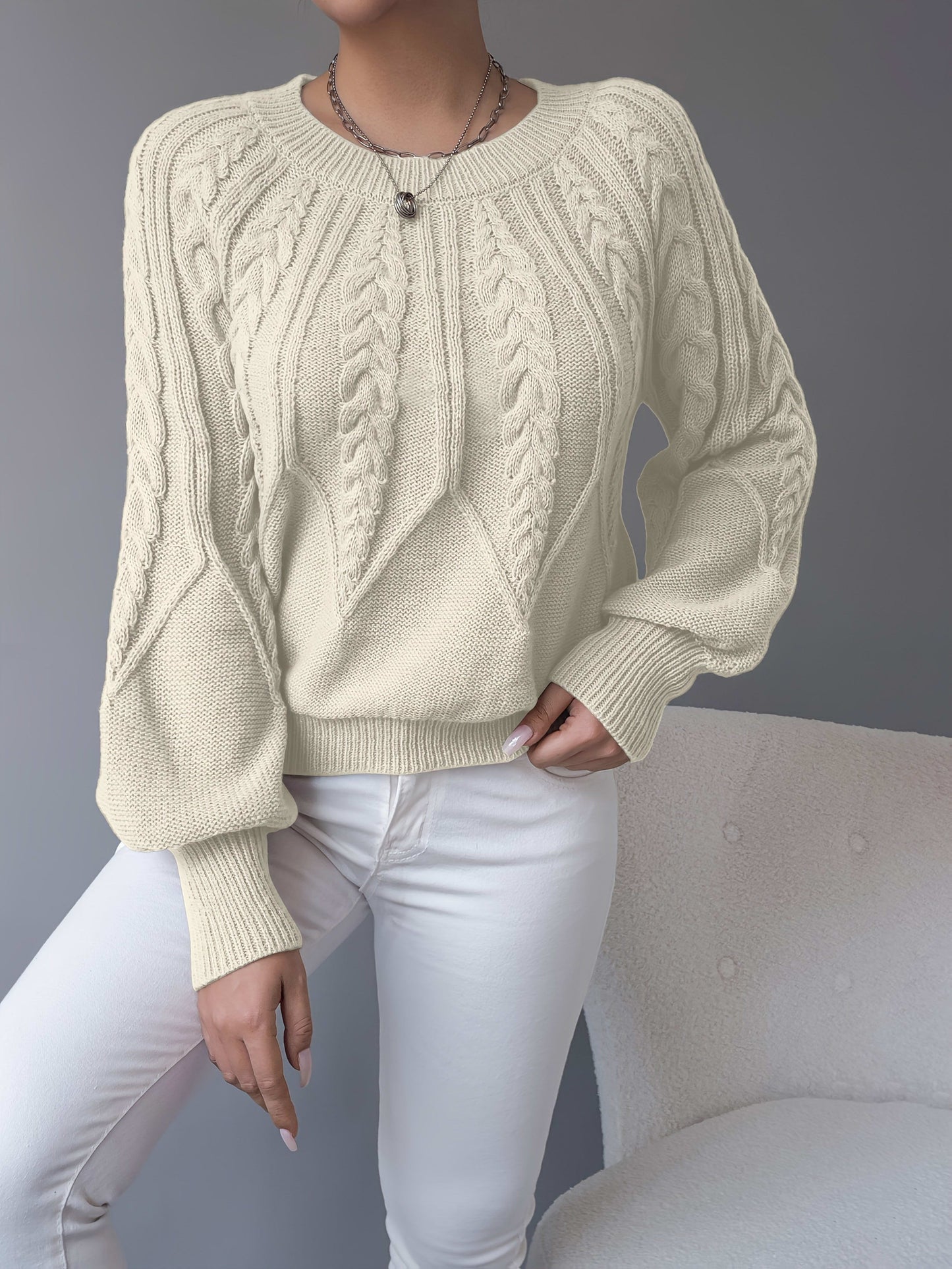 Kvinde iført en beige strikket sweater med kabelmonster og ballonærmer kombineret med hvide bukser_13