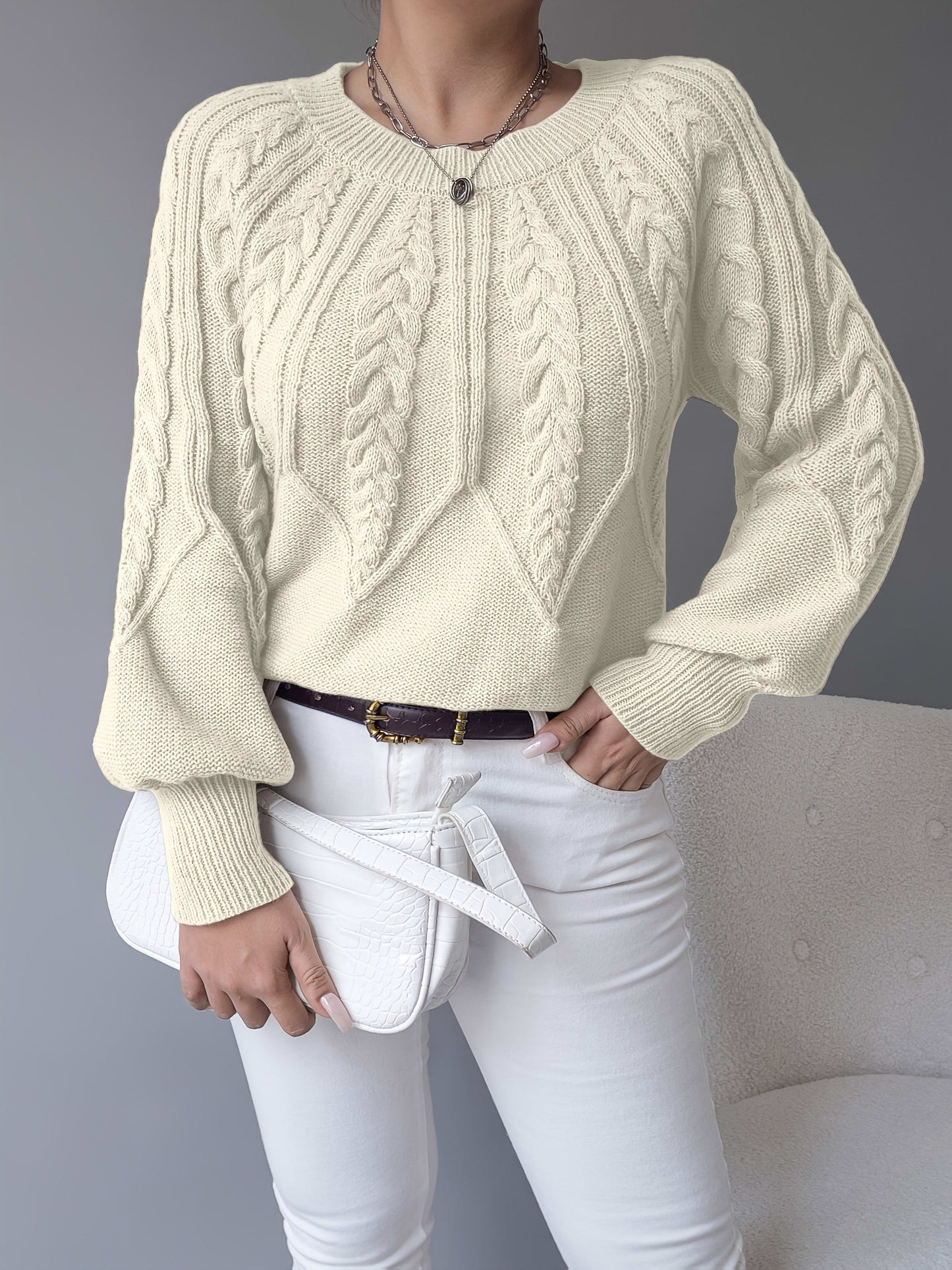 Kvinde iført en beige strikket sweater med kabelmonster og ballonærmer kombineret med hvide bukser_14
