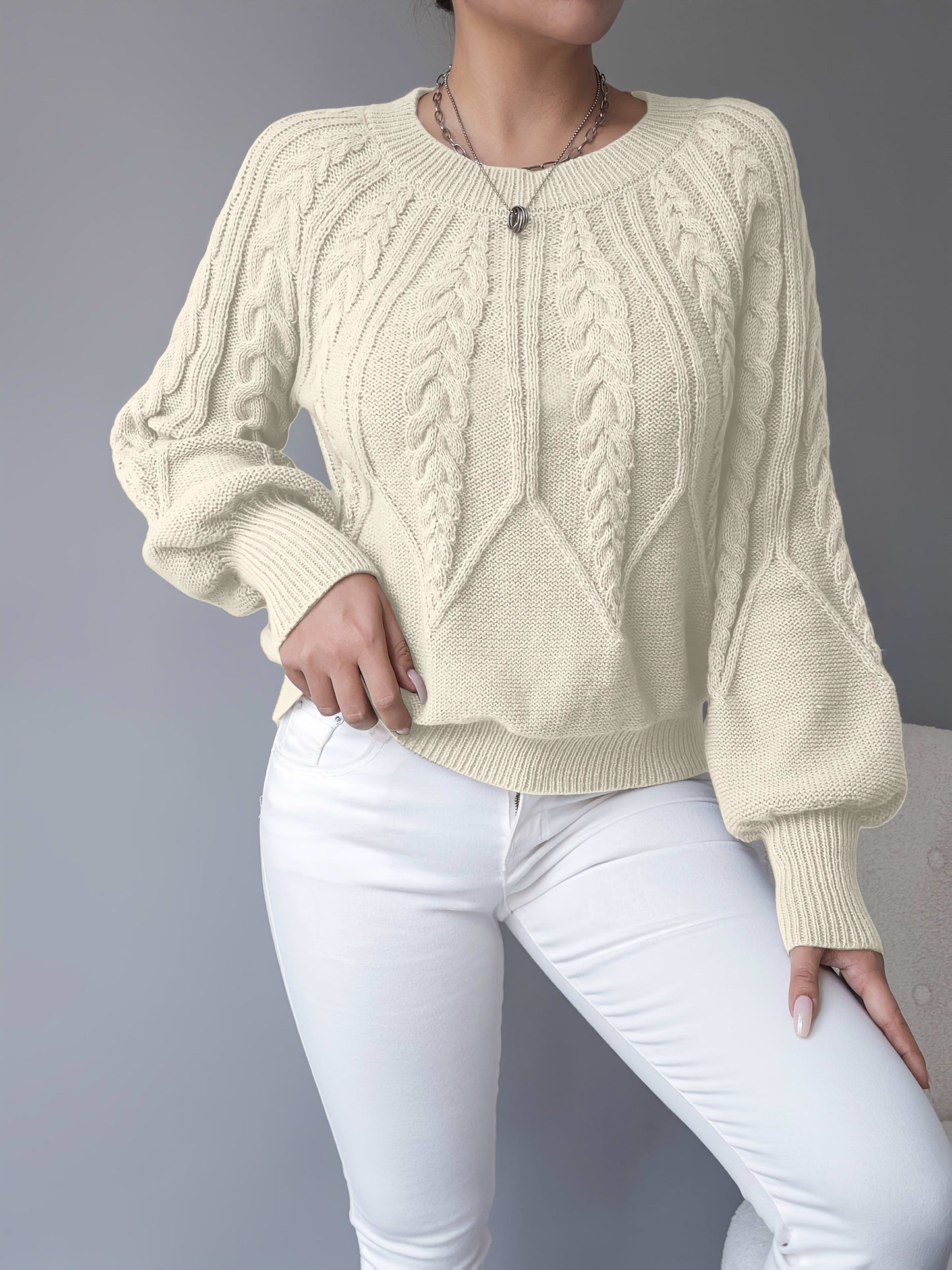 Kvinde iført en beige strikket sweater med kabelmonster og ballonærmer kombineret med hvide bukser_15