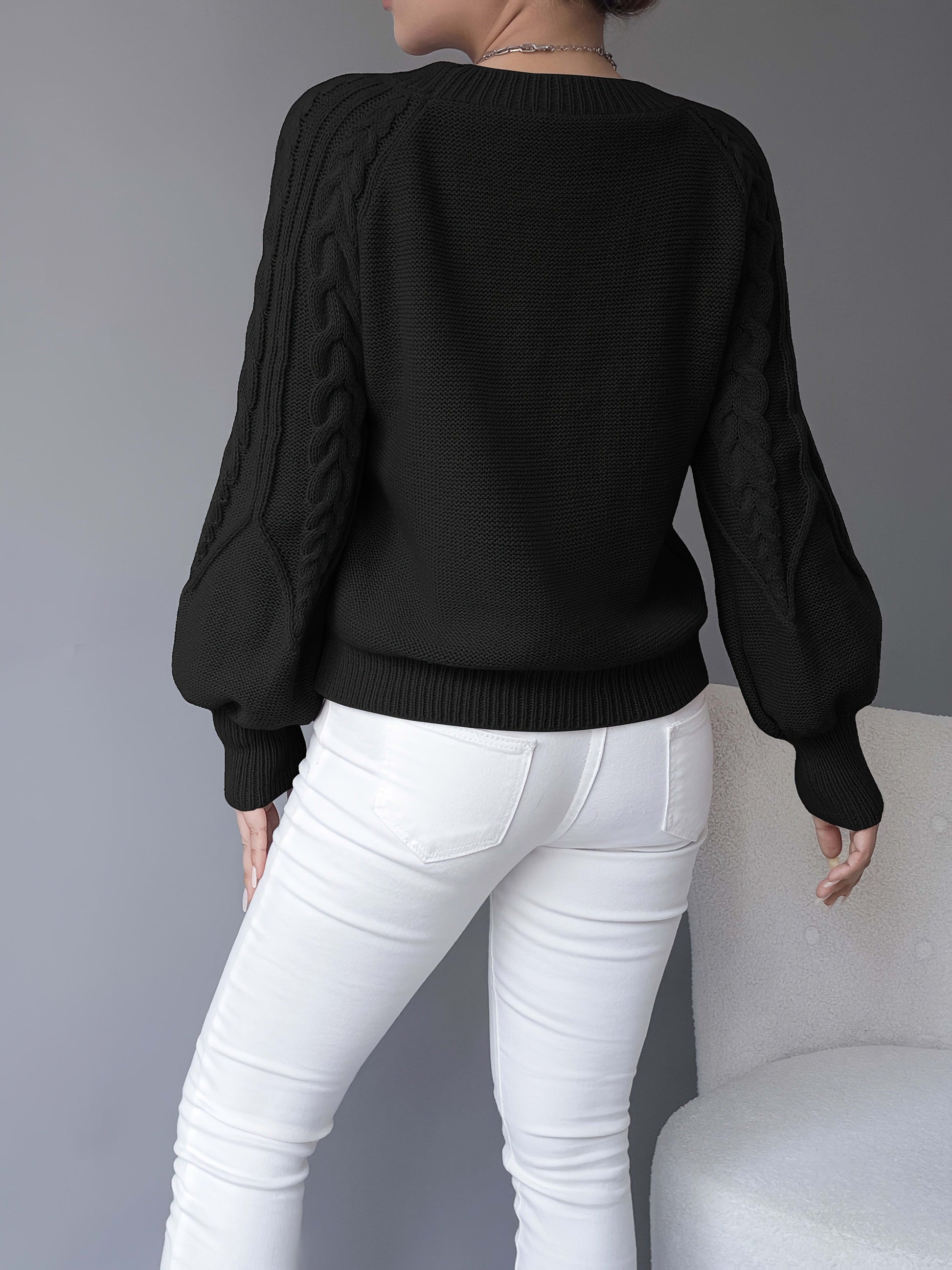 Kvinde iført en beige strikket sweater med kabelmonster og ballonærmer kombineret med hvide bukser_18
