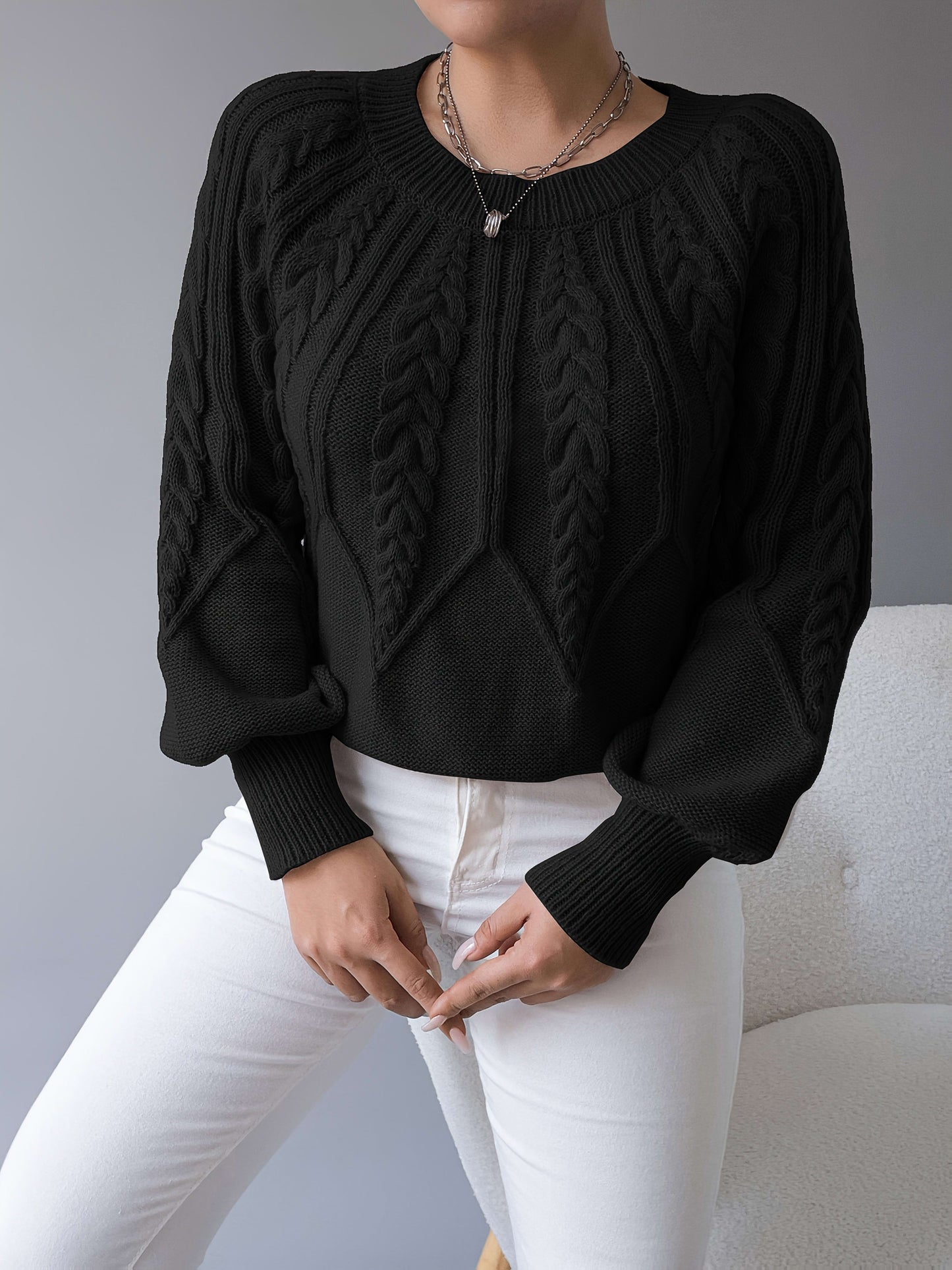 Kvinde iført en beige strikket sweater med kabelmonster og ballonærmer kombineret med hvide bukser_21