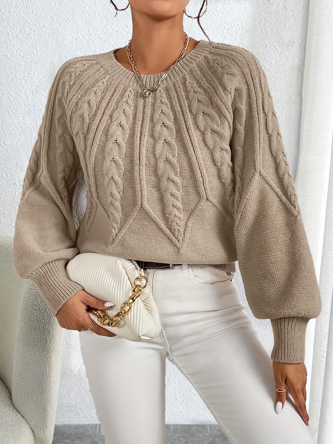 Kvinde iført en beige strikket sweater med kabelmonster og ballonærmer kombineret med hvide bukser_3