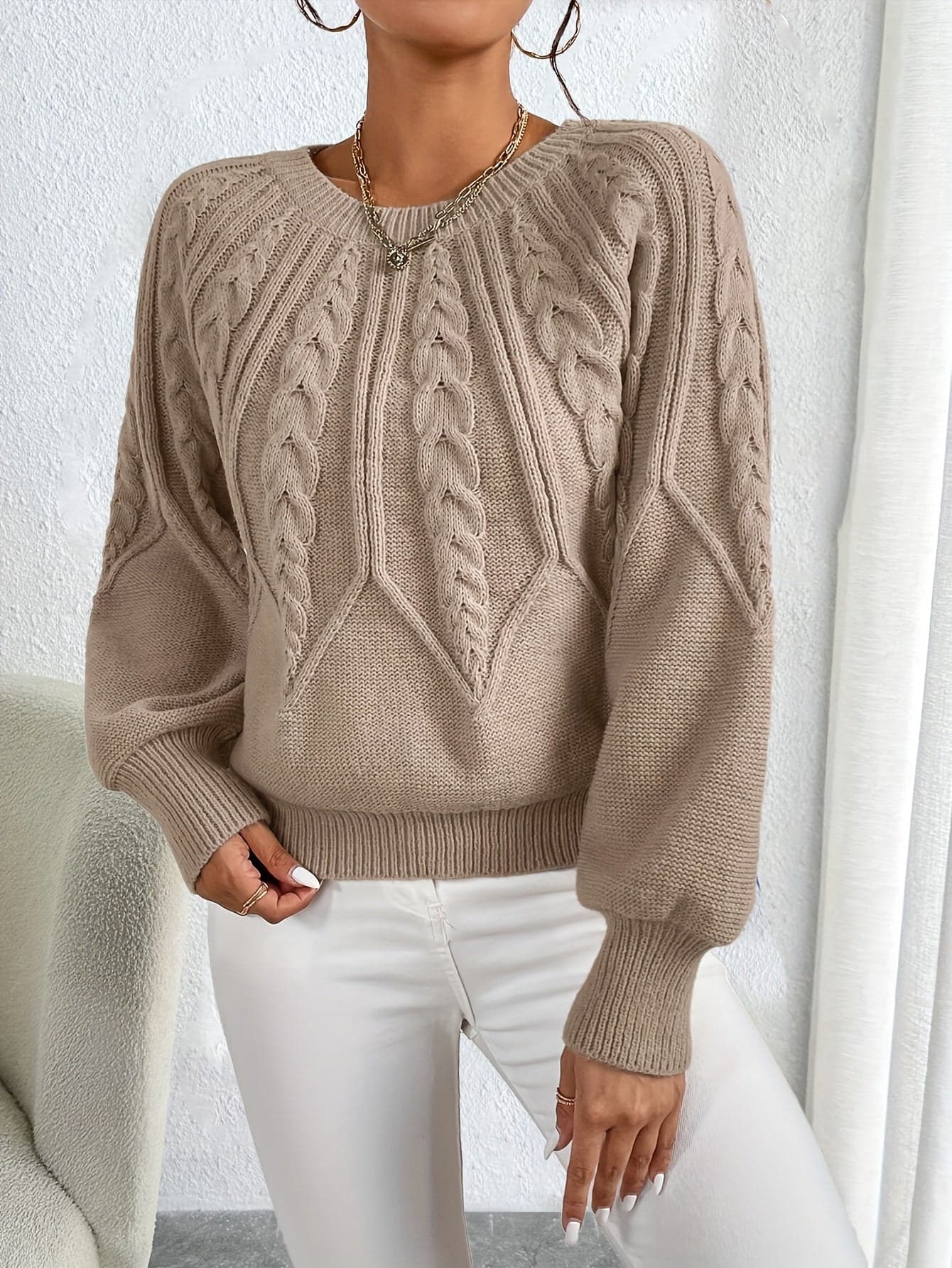 Kvinde iført en beige strikket sweater med kabelmonster og ballonærmer kombineret med hvide bukser_6