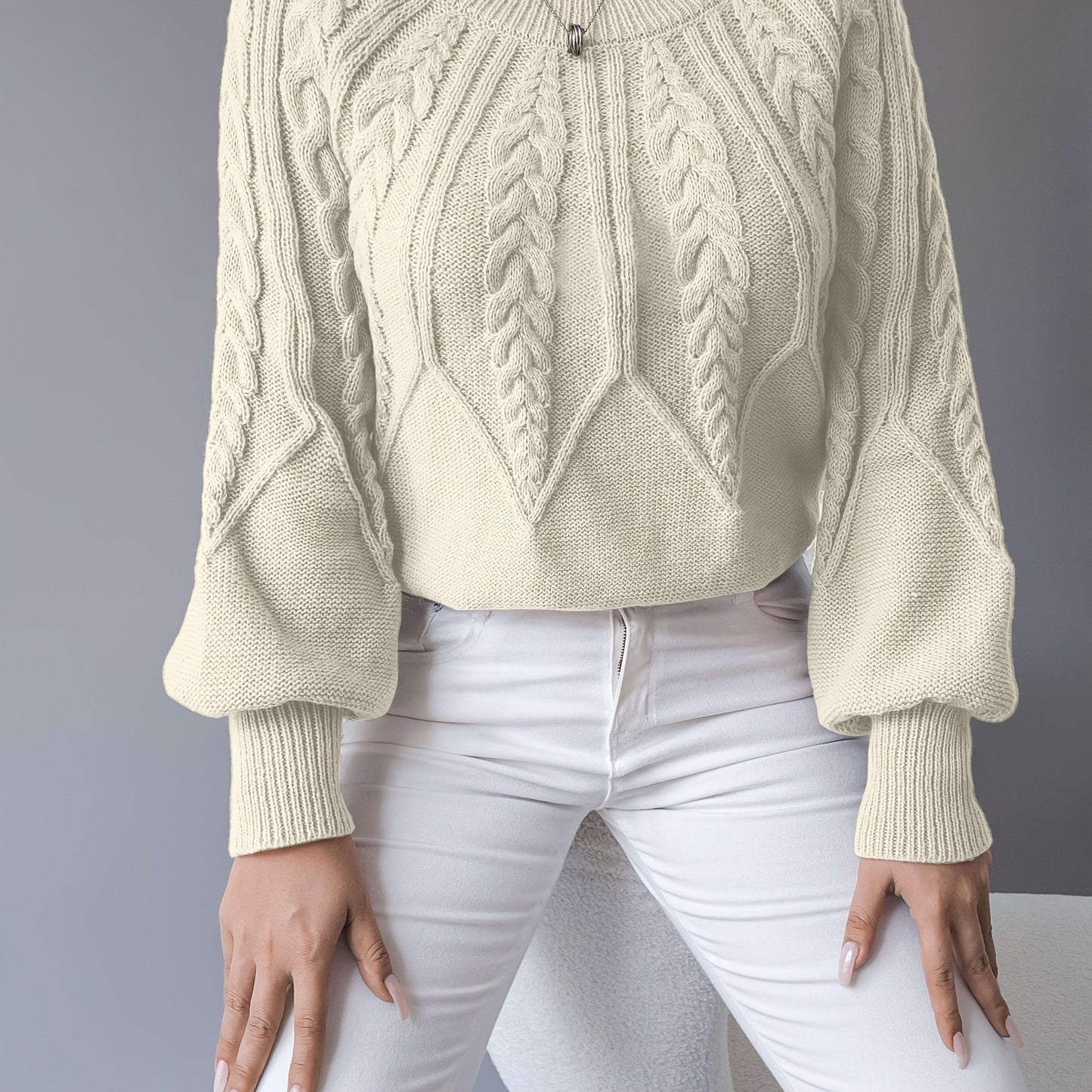 Kvinde iført en beige strikket sweater med kabelmonster og ballonærmer kombineret med hvide bukser_7
