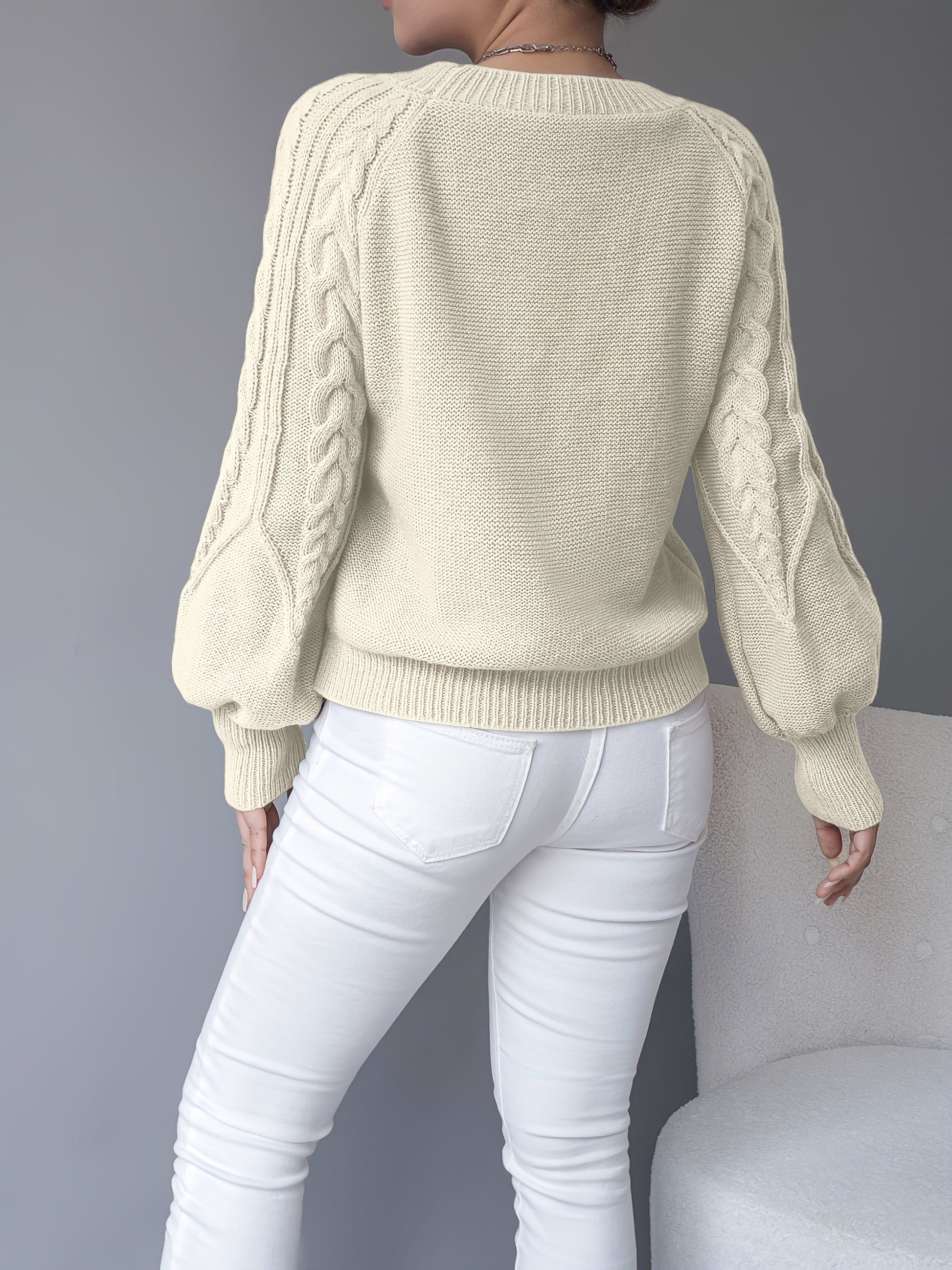 Kvinde iført en beige strikket sweater med kabelmonster og ballonærmer kombineret med hvide bukser_9