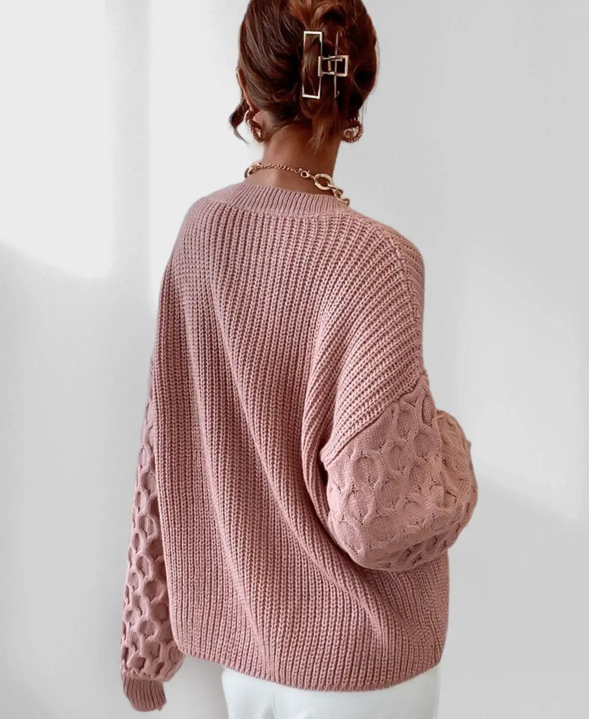 Model iført en grå strikket sweater med ballonærmer og kabelmønster sammen med lyse jeans og en guldfarvet kædehalskæde._10