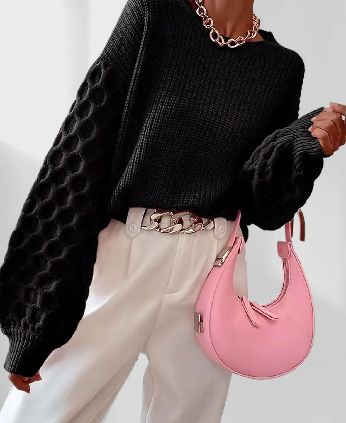 Model iført en grå strikket sweater med ballonærmer og kabelmønster sammen med lyse jeans og en guldfarvet kædehalskæde._11