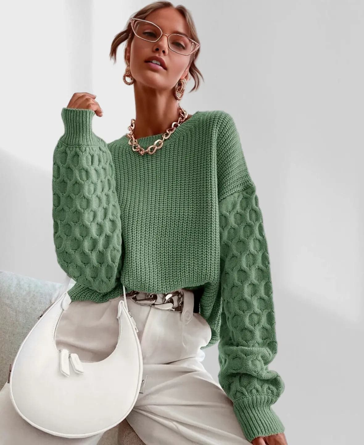 Model iført en grå strikket sweater med ballonærmer og kabelmønster sammen med lyse jeans og en guldfarvet kædehalskæde._12