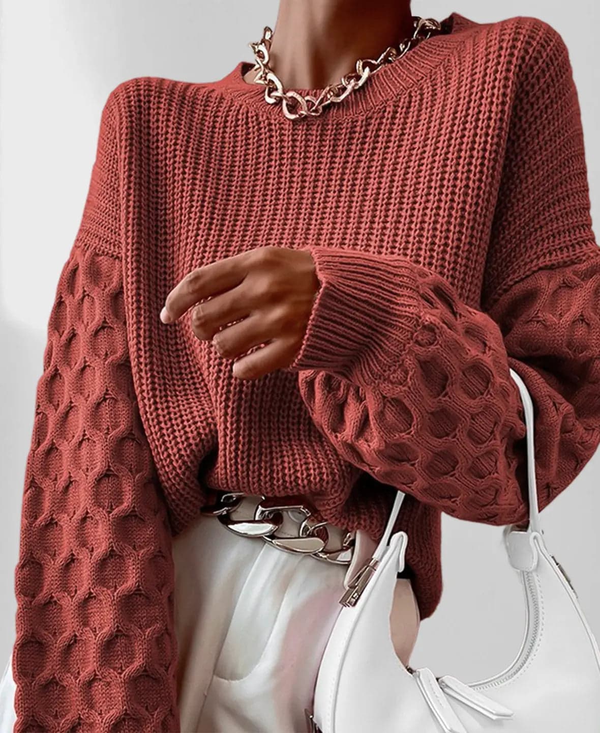 Model iført en grå strikket sweater med ballonærmer og kabelmønster sammen med lyse jeans og en guldfarvet kædehalskæde._7