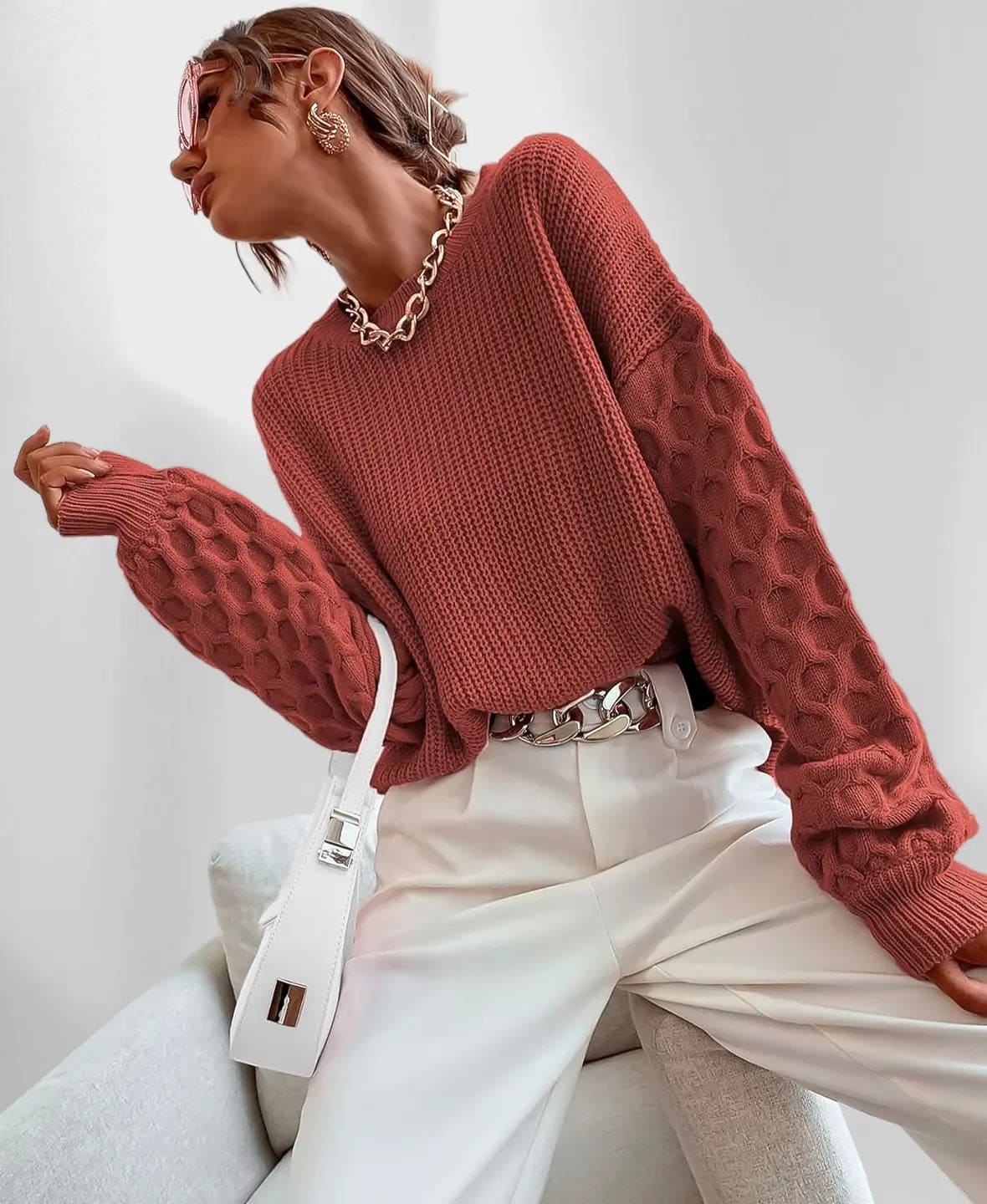 Model iført en grå strikket sweater med ballonærmer og kabelmønster sammen med lyse jeans og en guldfarvet kædehalskæde._8