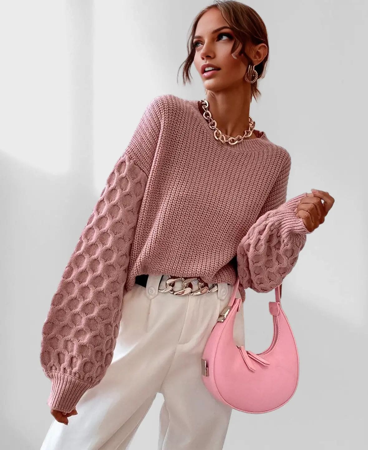 Model iført en grå strikket sweater med ballonærmer og kabelmønster sammen med lyse jeans og en guldfarvet kædehalskæde._9