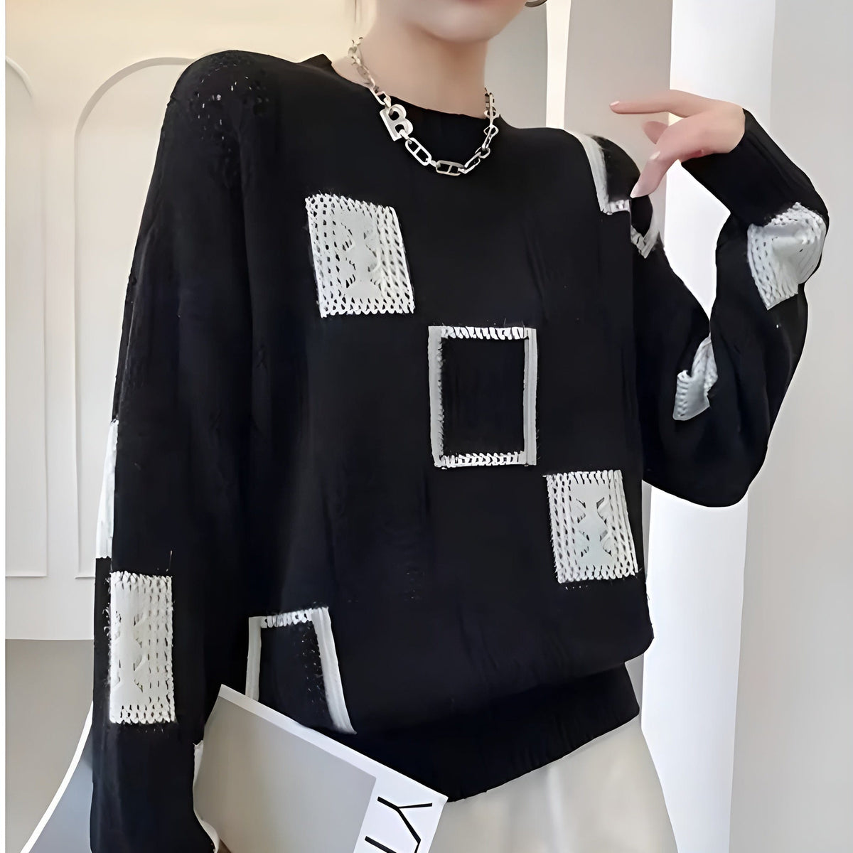 Kvinde iført hvid strikket sweater med sorte geometriske blokke i grafisk mønster og rund hals._5