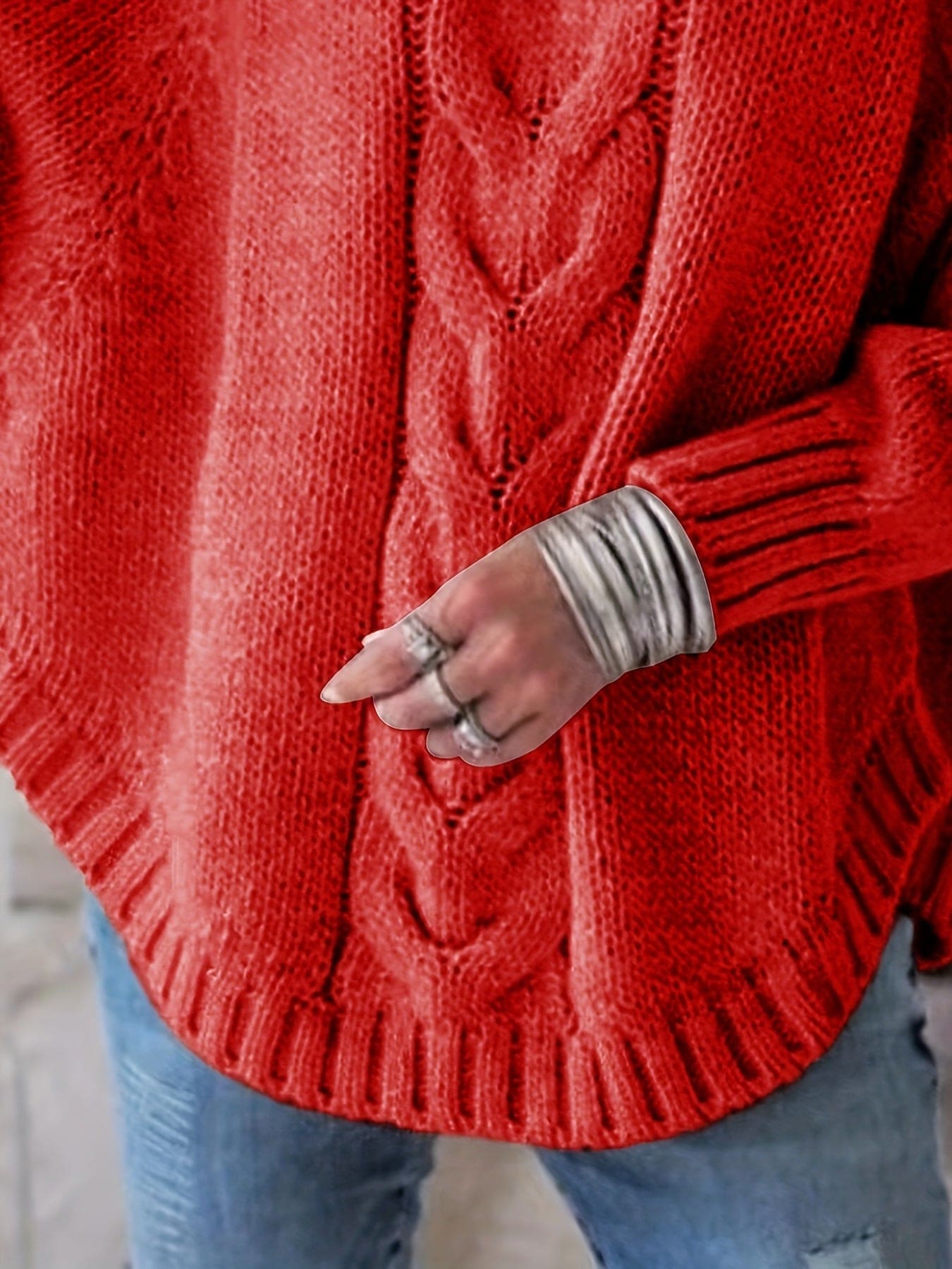 Kvinde iført grå strikket sweater med høj hals og kabelmønster, stylet med sølvfarvede armbånd og lyse jeans._10