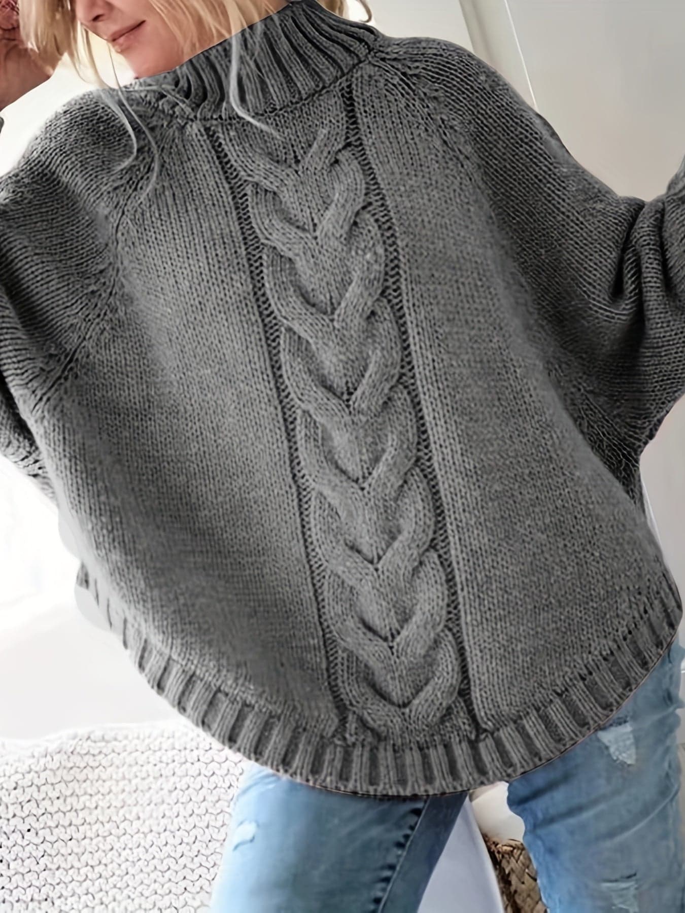 Kvinde iført grå strikket sweater med høj hals og kabelmønster, stylet med sølvfarvede armbånd og lyse jeans._2