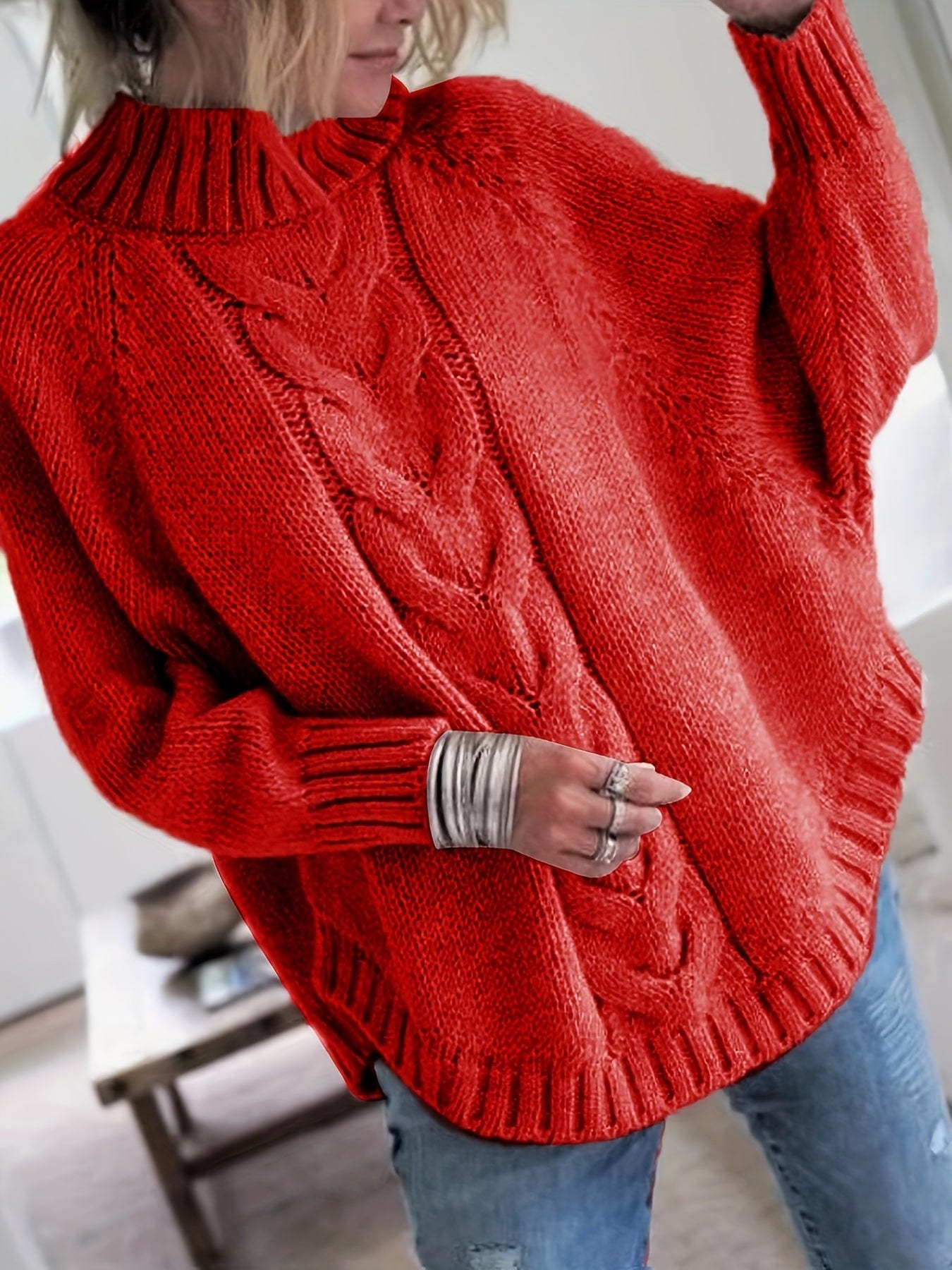 Kvinde iført grå strikket sweater med høj hals og kabelmønster, stylet med sølvfarvede armbånd og lyse jeans._9