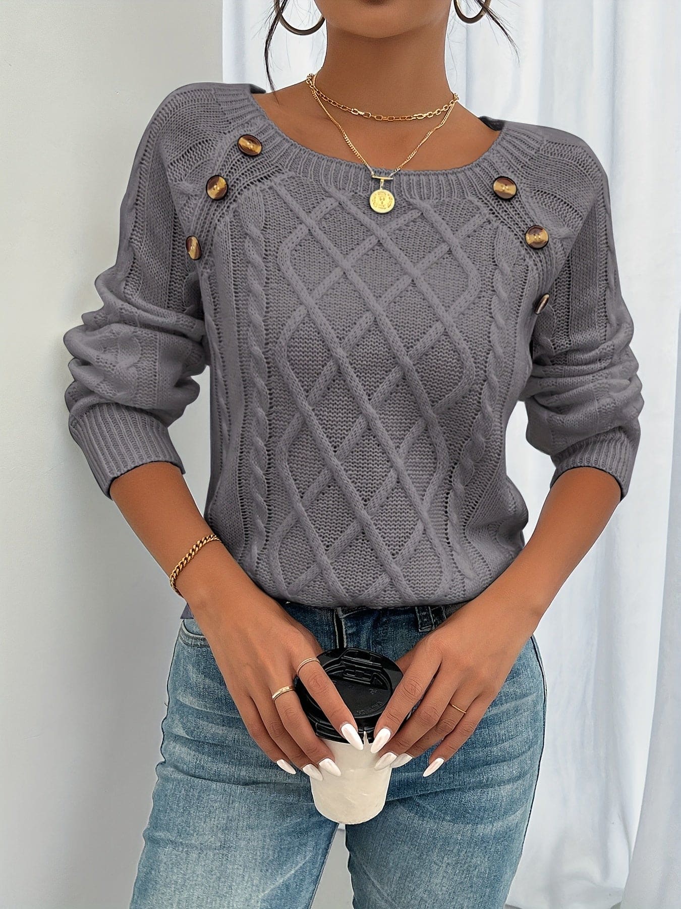Kvinde iført beige strikket sweater med kabelstruktur og knapper ved skulderen, kombineret med lyse jeans_1