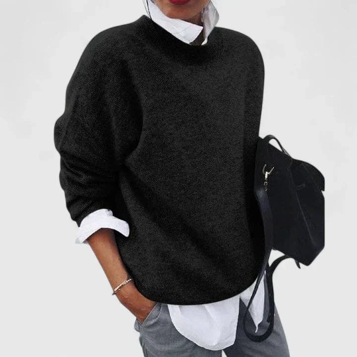 Kvinde iført mørk oversize sweater over hvid skjorte med grå bukser og sort taske._0