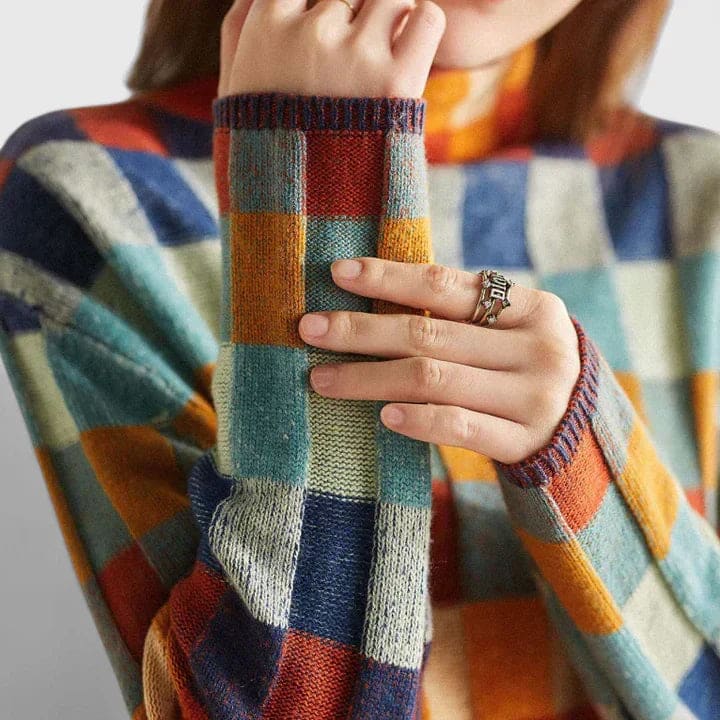 Kvinde iført sweater med farverigt ternmønster i blå, orange, rød og grøn nuancer, stylet med hvide bukser_1