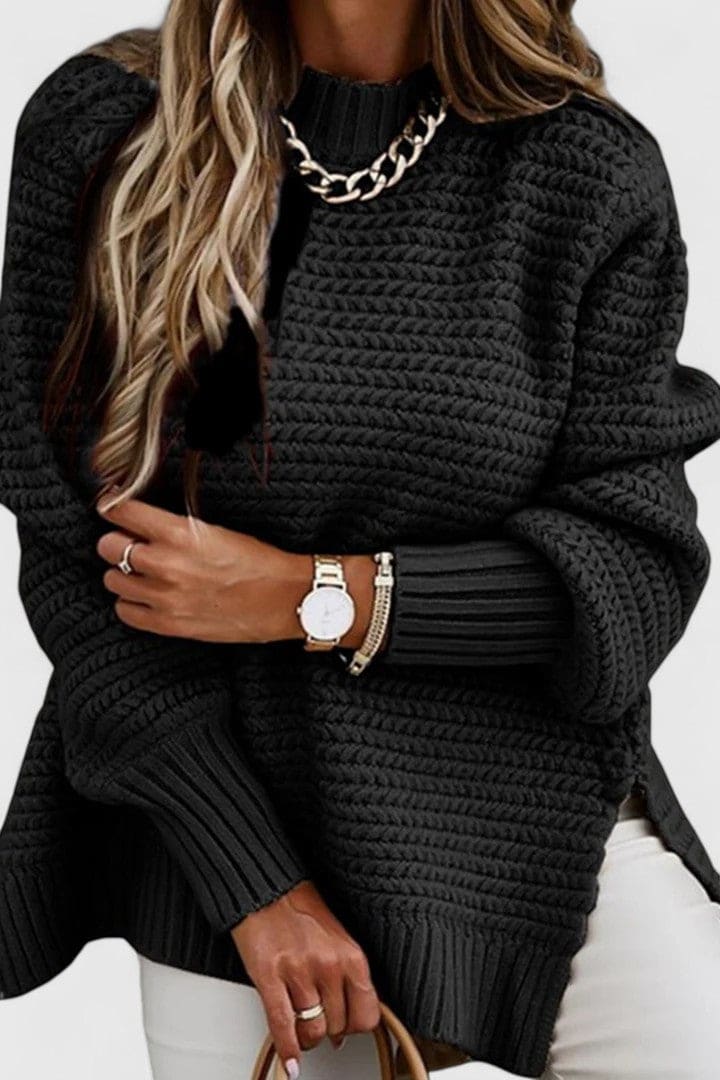 Kvinde iført en sort sweater med struktureret strik, rund hals og løs pasform, stylet med armbåndsur og halskæde._0