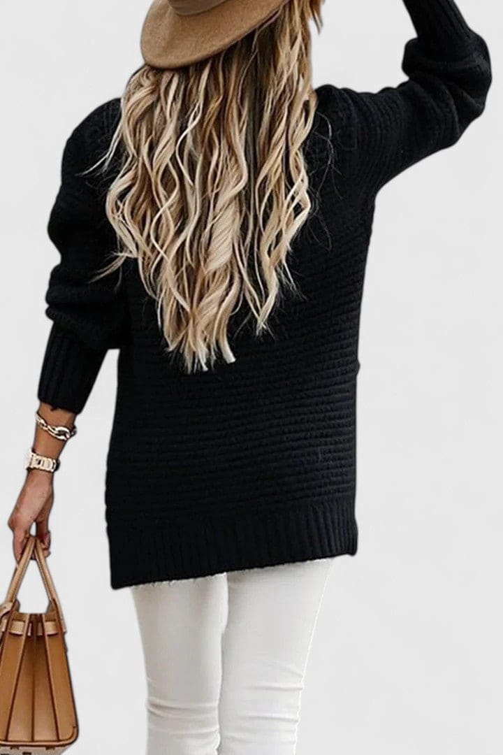 Kvinde iført en sort sweater med struktureret strik, rund hals og løs pasform, stylet med armbåndsur og halskæde._1