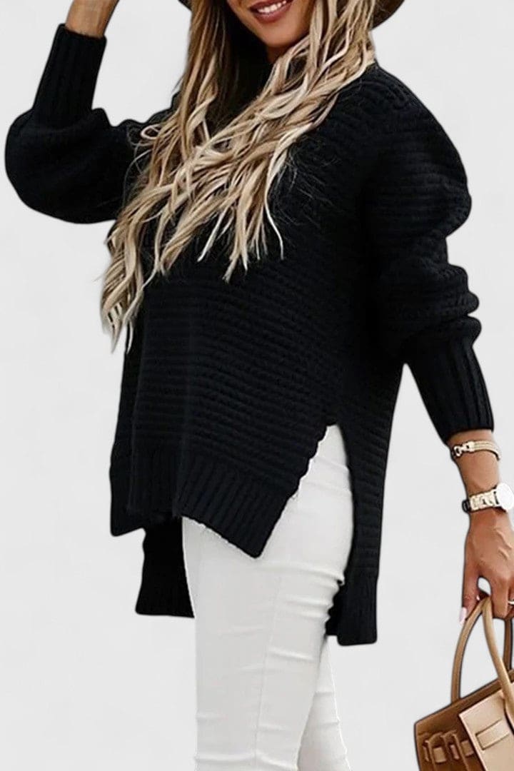 Kvinde iført en sort sweater med struktureret strik, rund hals og løs pasform, stylet med armbåndsur og halskæde._2