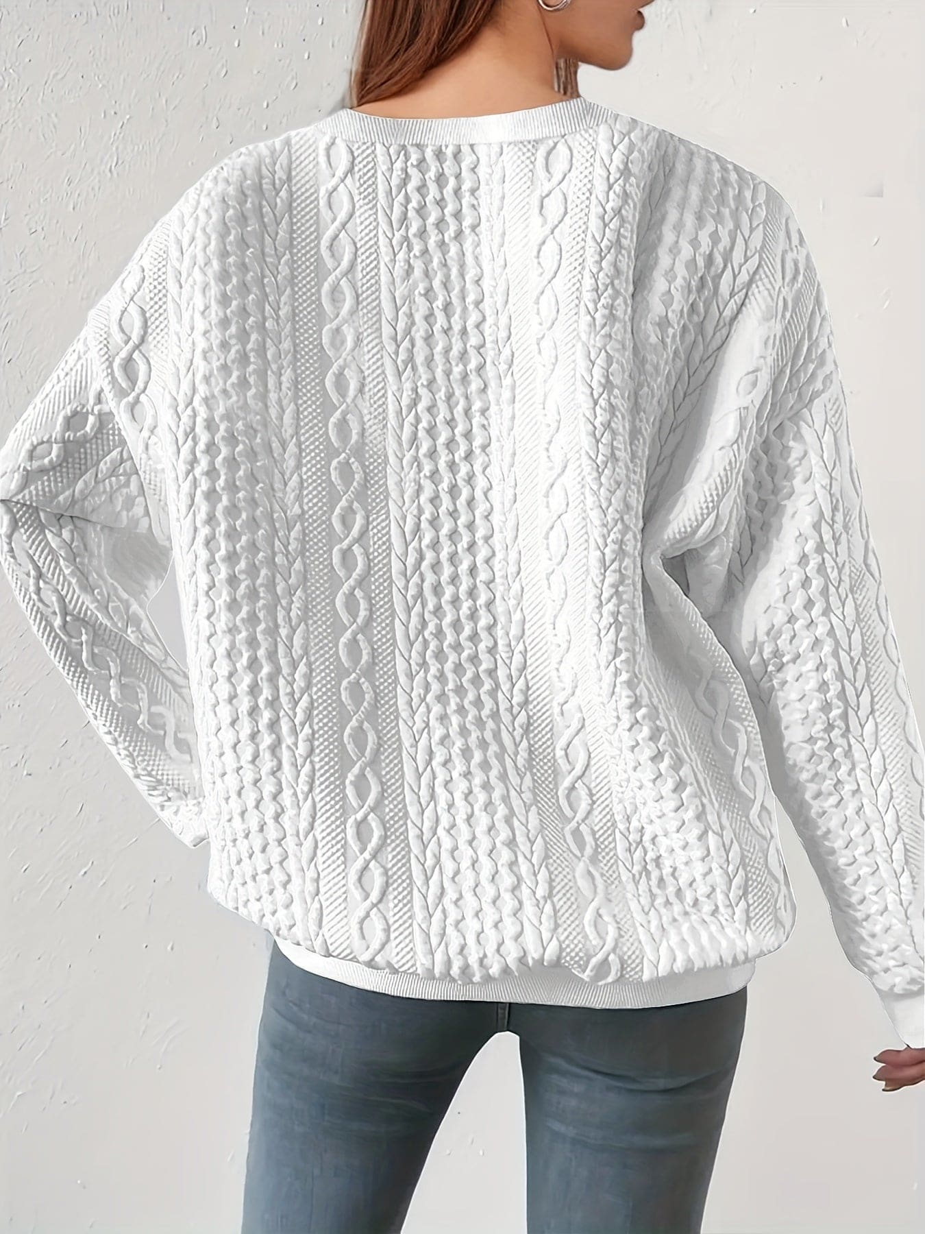 Hvid sweatshirt med struktureret kabelstriksmønster, fotograferet på model mod neutral baggrund._1
