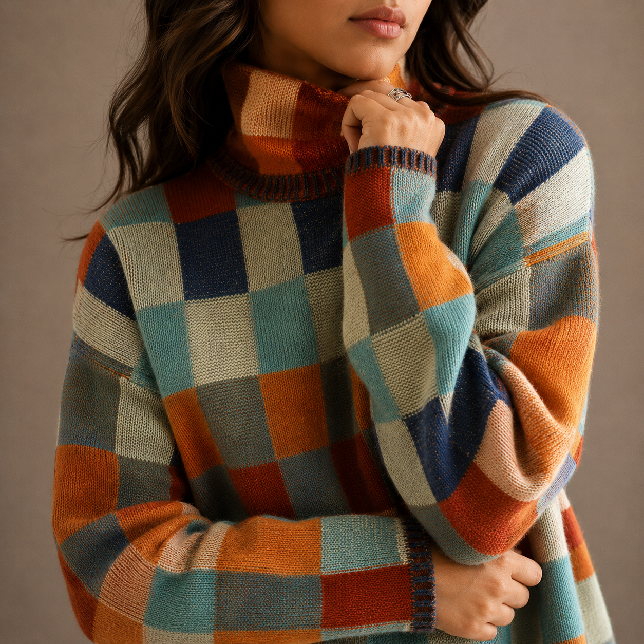 Model iført en ternet sweater med høj hals i orange, blå og beige nuancer, stylet med sorte bukser_1
