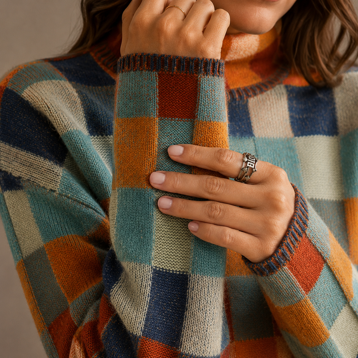 Model iført en ternet sweater med høj hals i orange, blå og beige nuancer, stylet med sorte bukser_2