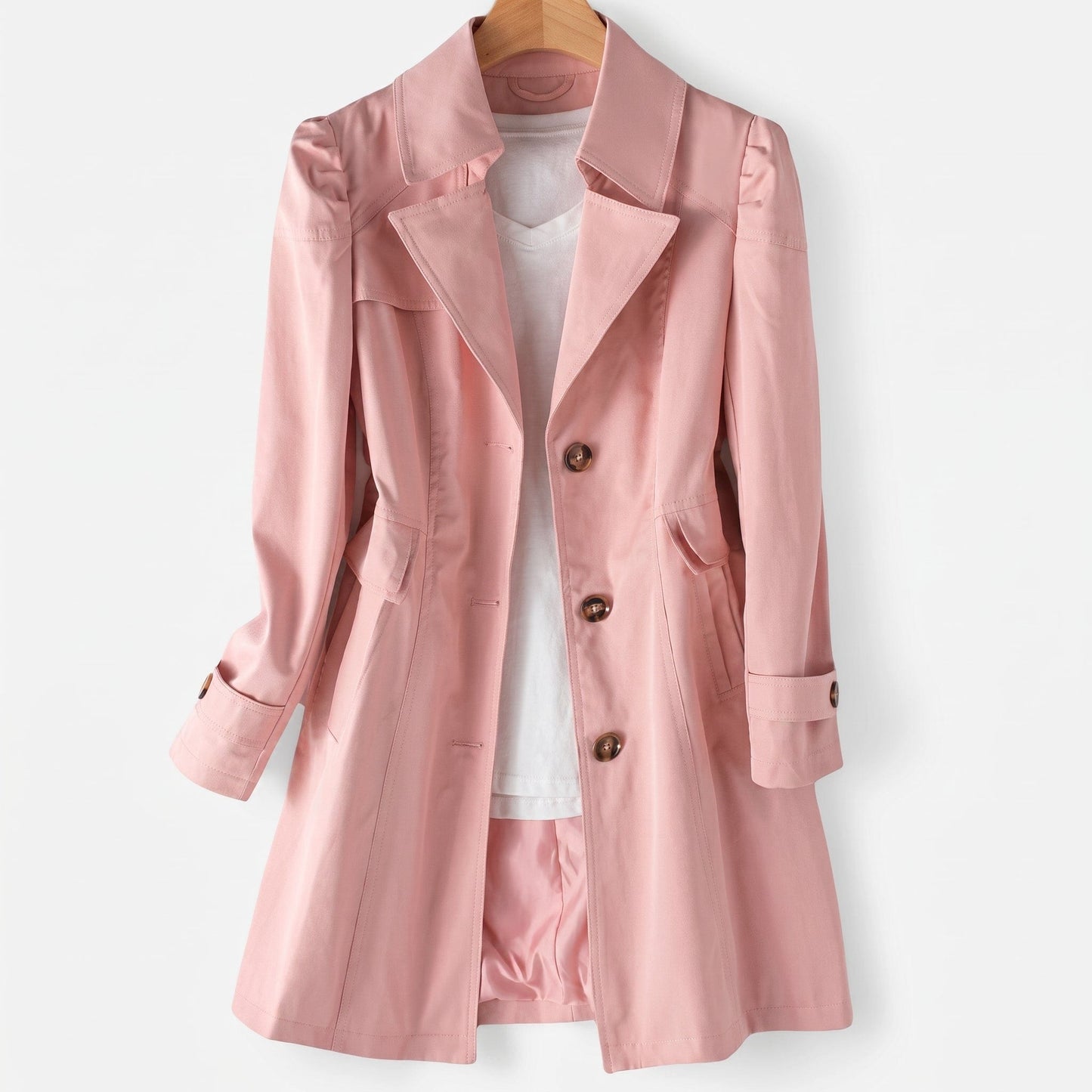 Rosa trenchcoat med klassisk revers, knaplukning og skræddersyet pasform hængende på bøjle over hvid top_0