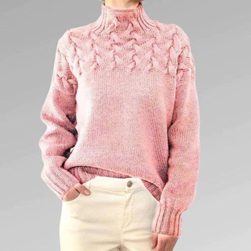 Kvinde iført rosa turtleneck sweater med kabelstrik detalje over skuldrene og oversize pasform, kombineret med hvide bukser._0