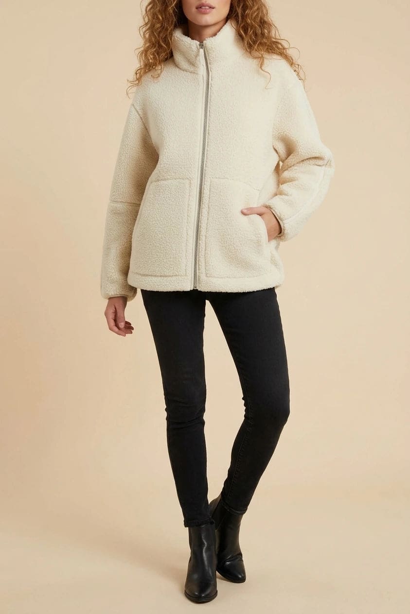 Kvinde i hoftelang teddyjakke med gennemgående lynlås, høj krave og to påsatte lommer, styret med sorte jeans og ankelstøvler._0