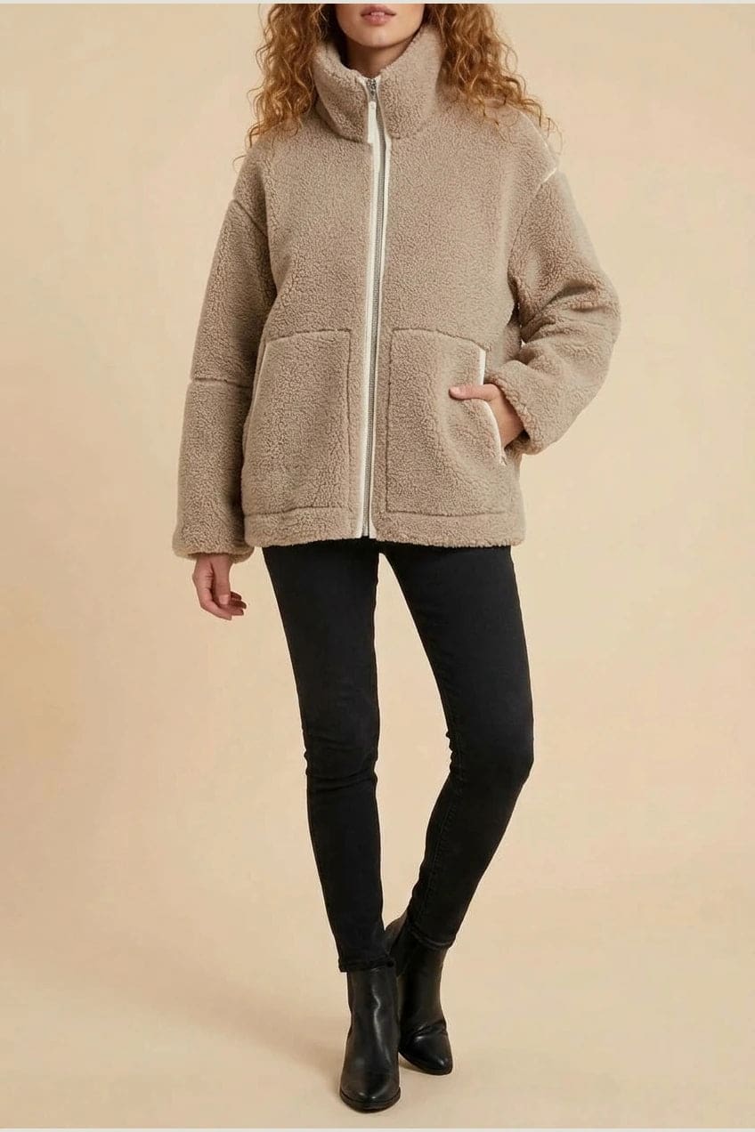 Kvinde i hoftelang teddyjakke med gennemgående lynlås, høj krave og to påsatte lommer, styret med sorte jeans og ankelstøvler._1