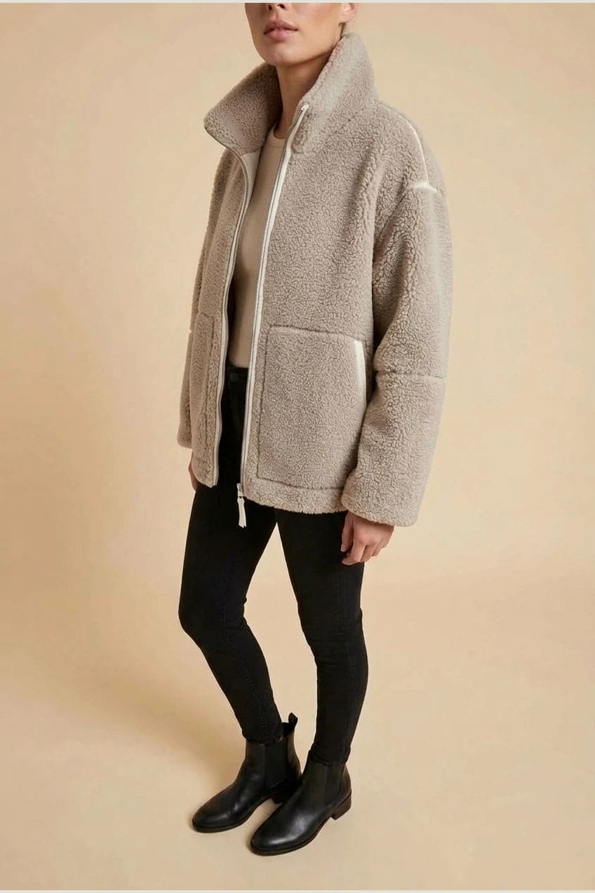 Kvinde i hoftelang teddyjakke med gennemgående lynlås, høj krave og to påsatte lommer, styret med sorte jeans og ankelstøvler._3